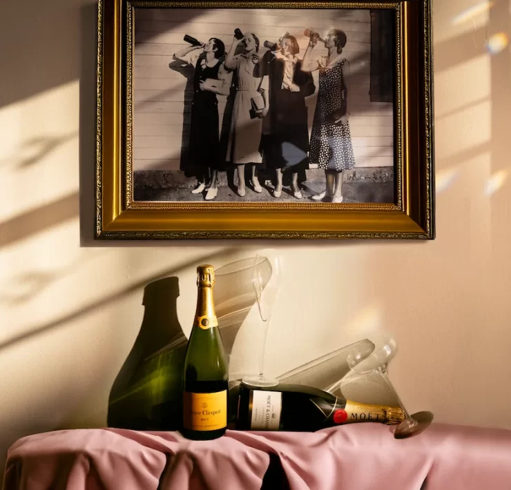 Framed vintage photo of women drinking champagne, with Veuve Clicquot and Moët bottles and glassware on a pink-draped table