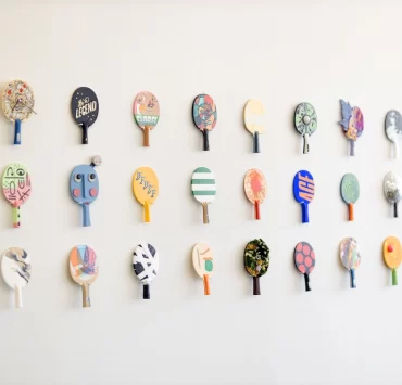 Wall display of colourful, artist-designed table tennis paddles at the TOPSP!N exhibition in Glasgow