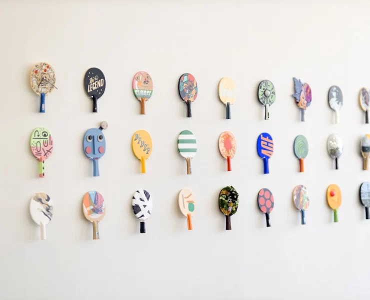 Wall display of colourful, artist-designed table tennis paddles at the TOPSP!N exhibition in Glasgow