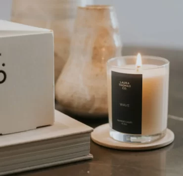 Lit 'Wave' candle by Laura Thomas Co. sits on a coaster next to ceramic vases and a branded LT.CO box.