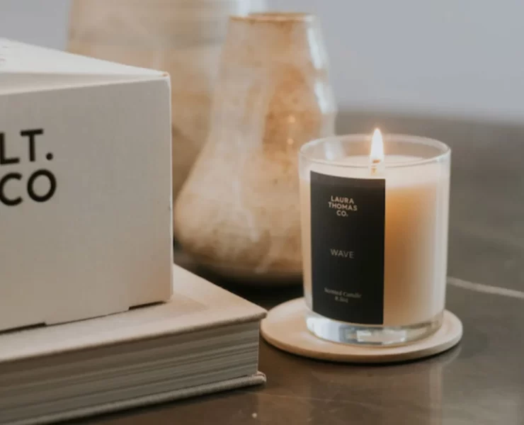 Lit 'Wave' candle by Laura Thomas Co. sits on a coaster next to ceramic vases and a branded LT.CO box.