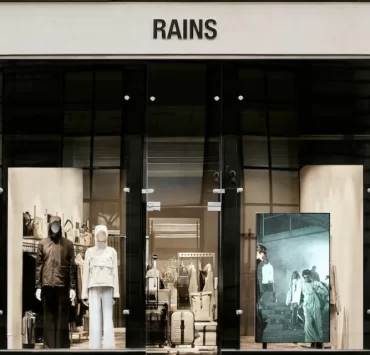 Exterior of the Rains store on Ingram Street, Glasgow, with modern window displays and mannequins in rainwear.