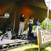 Folk musicians perform onstage at The Reeling Festival in Glasgow, under a canopy tent at Rouken Glen Park.