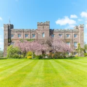 Wide shot of Scone Palace with pink cherry trees and striped green lawn under a clear blue Scottish sky