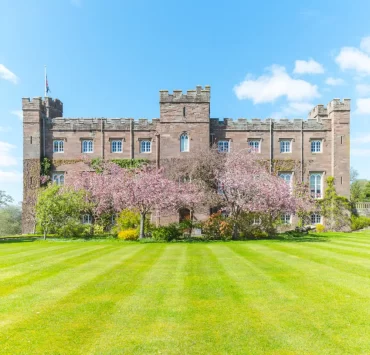 Wide shot of Scone Palace with pink cherry trees and striped green lawn under a clear blue Scottish sky