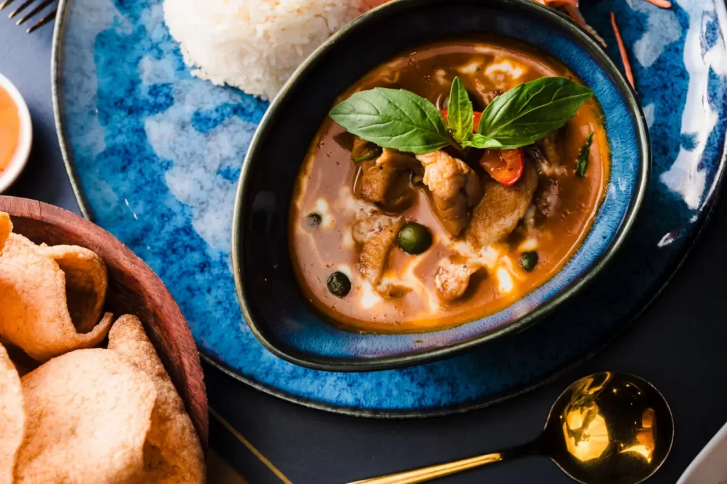 Bowl of red Thai curry with chicken, fresh basil, and coconut milk served with jasmine rice and prawn crackers at The Thai, Shawlands
