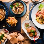 Flat lay of Thai dishes at The Thai in Shawlands, Glasgow, featuring curries, stir-fries, spring rolls, rice, and cocktails on a wooden table