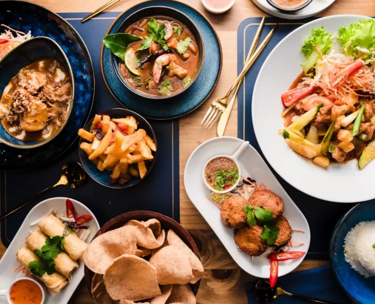 Flat lay of Thai dishes at The Thai in Shawlands, Glasgow, featuring curries, stir-fries, spring rolls, rice, and cocktails on a wooden table
