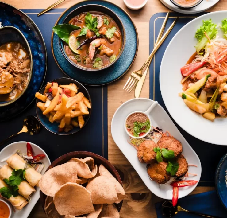Flat lay of Thai dishes at The Thai in Shawlands, Glasgow, featuring curries, stir-fries, spring rolls, rice, and cocktails on a wooden table