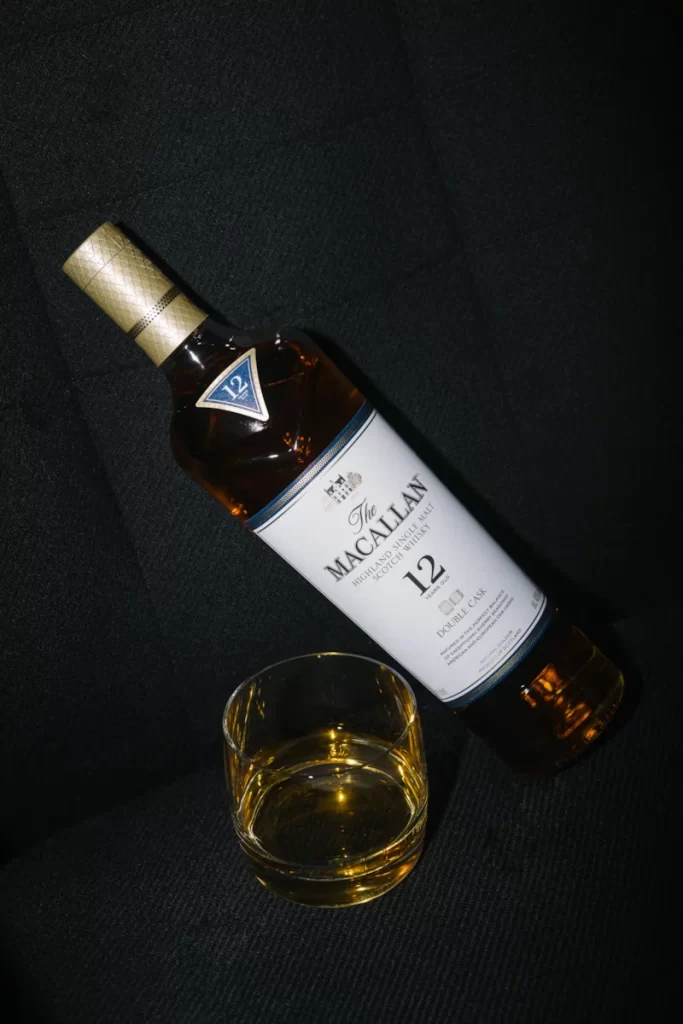 A bottle of The Macallan 12 Year Double Cask whisky with a glass on dark fabric.