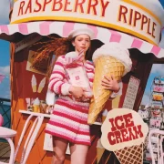 Model in pink striped outfit holding oversized raspberry ripple cone in front of Jo Malone ice cream stand.