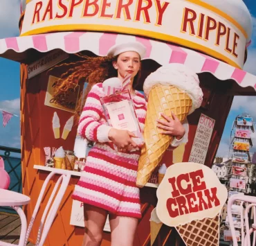 Model in pink striped outfit holding oversized raspberry ripple cone in front of Jo Malone ice cream stand.