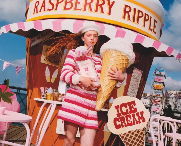 Model in pink striped outfit holding oversized raspberry ripple cone in front of Jo Malone ice cream stand.