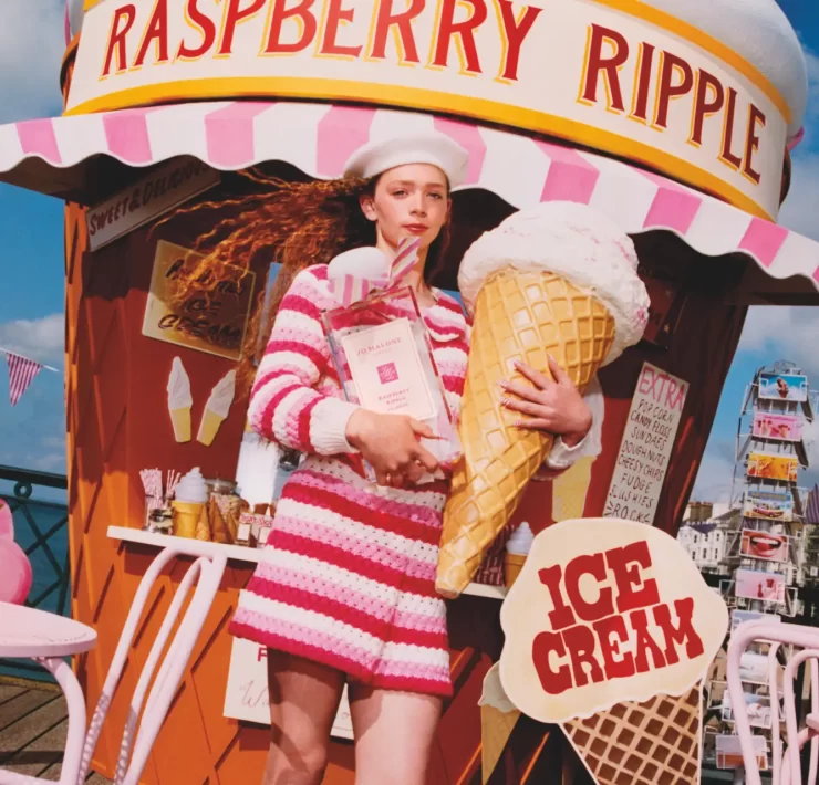 Model in pink striped outfit holding oversized raspberry ripple cone in front of Jo Malone ice cream stand.
