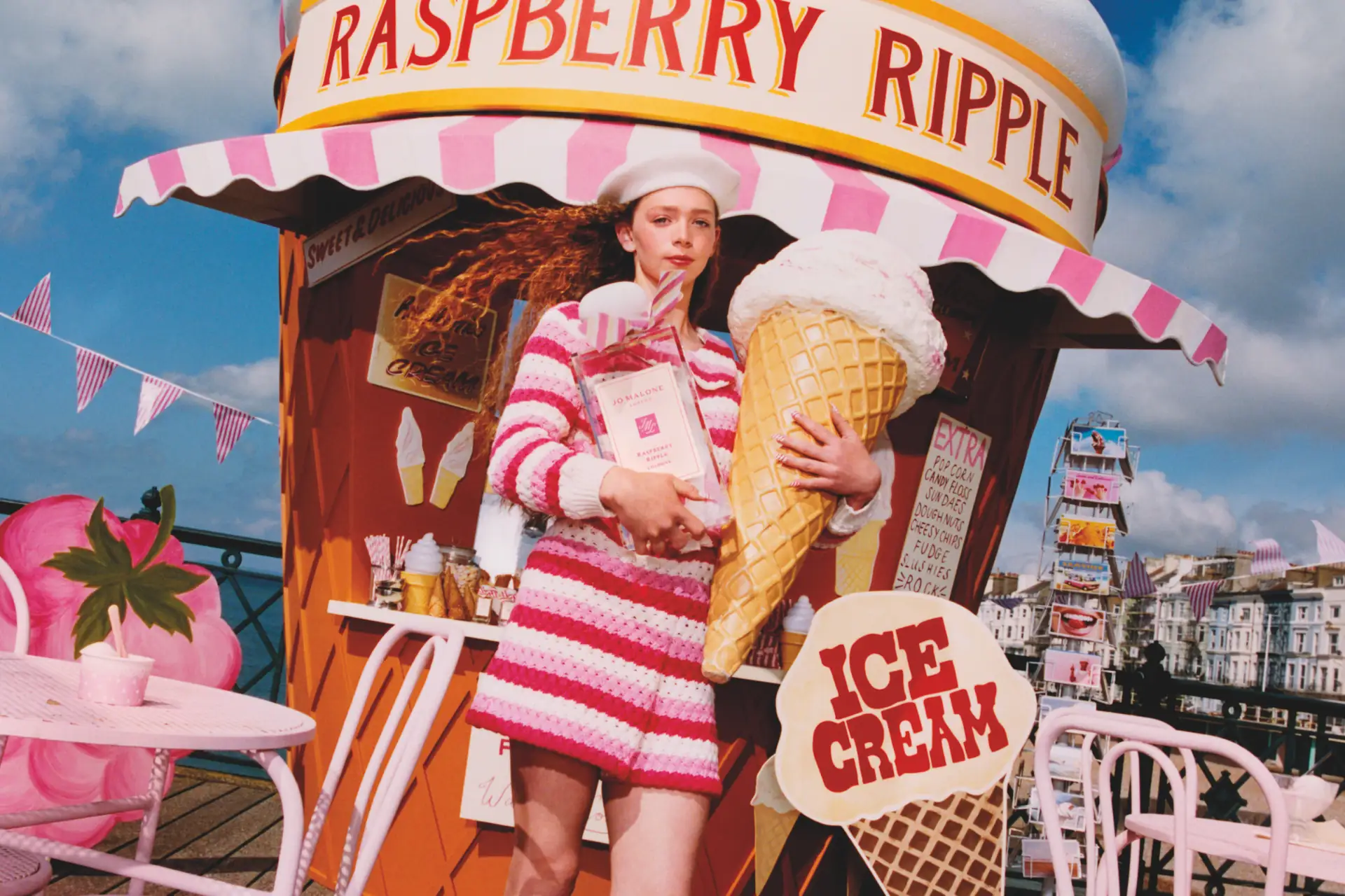 Model in pink striped outfit holding oversized raspberry ripple cone in front of Jo Malone ice cream stand.