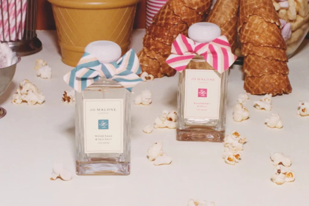 Jo Malone Raspberry Ripple and Wood Sage & Sea Salt colognes with striped bows among popcorn and cones.