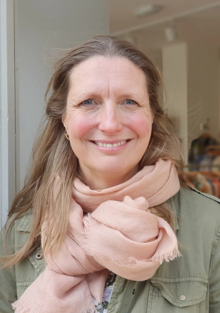 Smiling woman in pink scarf outside an independent fashion shop.
