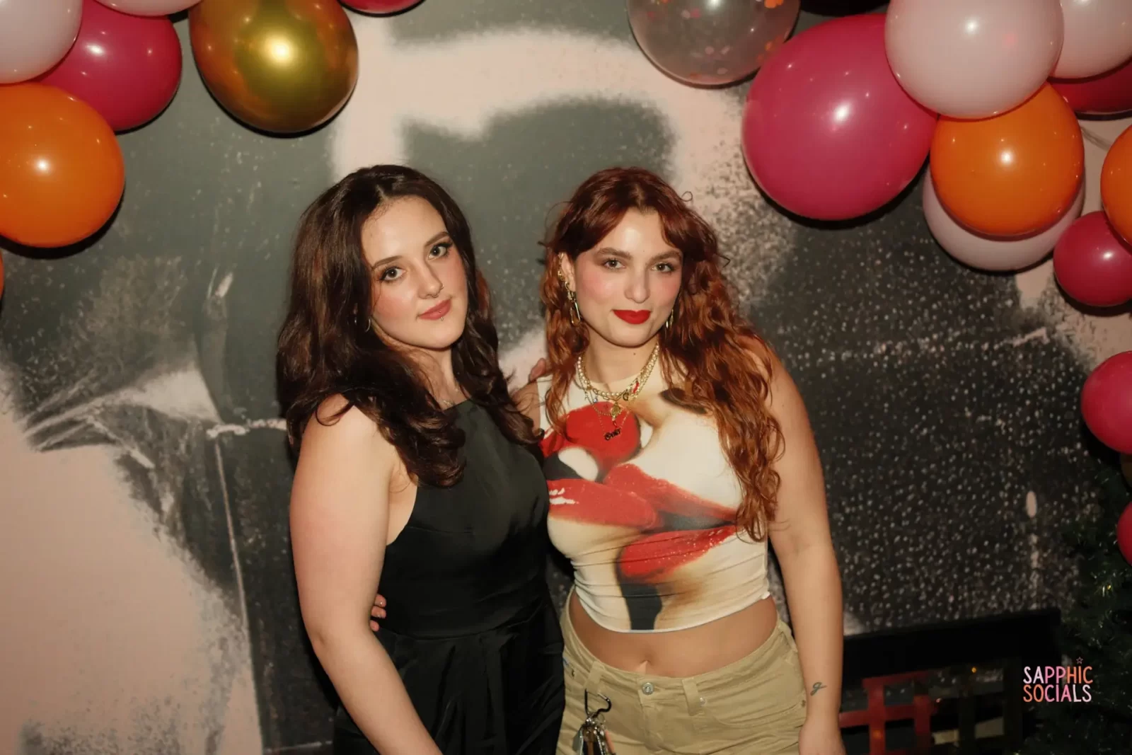 Ellie Devlin and Gaia Ragone, co-founders of The Sapphic Space, posing under colourful balloons at a Pride-themed event in Glasgow