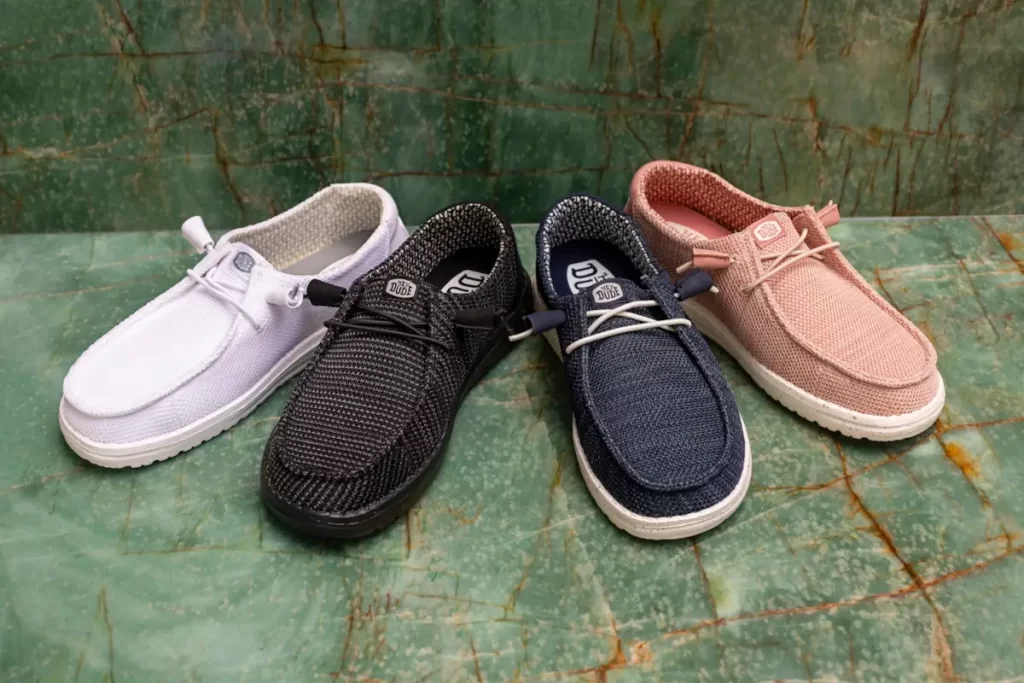 Four HEYDUDE Wally shoes in white, black, navy and blush on a green marble background