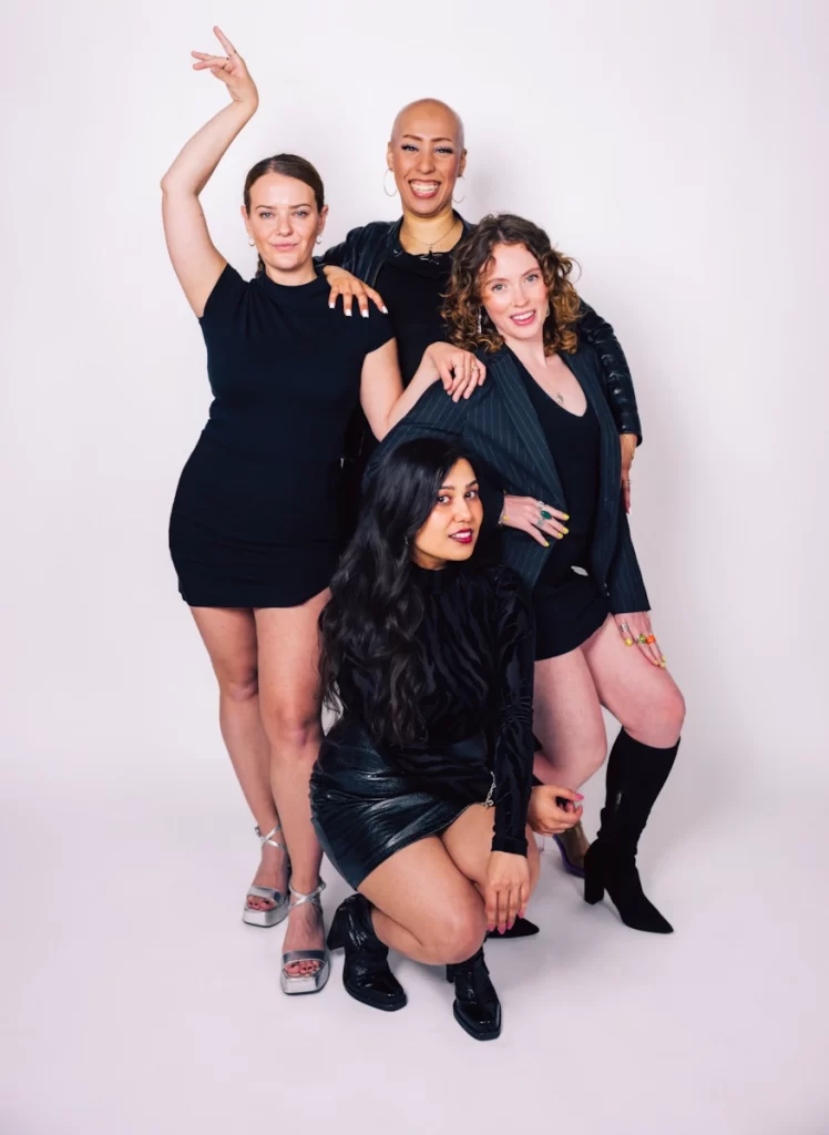 Four cast members of Girl Pop! pose confidently in black outfits against a white backdrop, ahead of their 2024 Edinburgh Fringe debut.