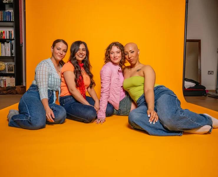 Four members of the Girl Pop! cast sitting together against a bright yellow backdrop, dressed in bold Y2K-inspired outfits.