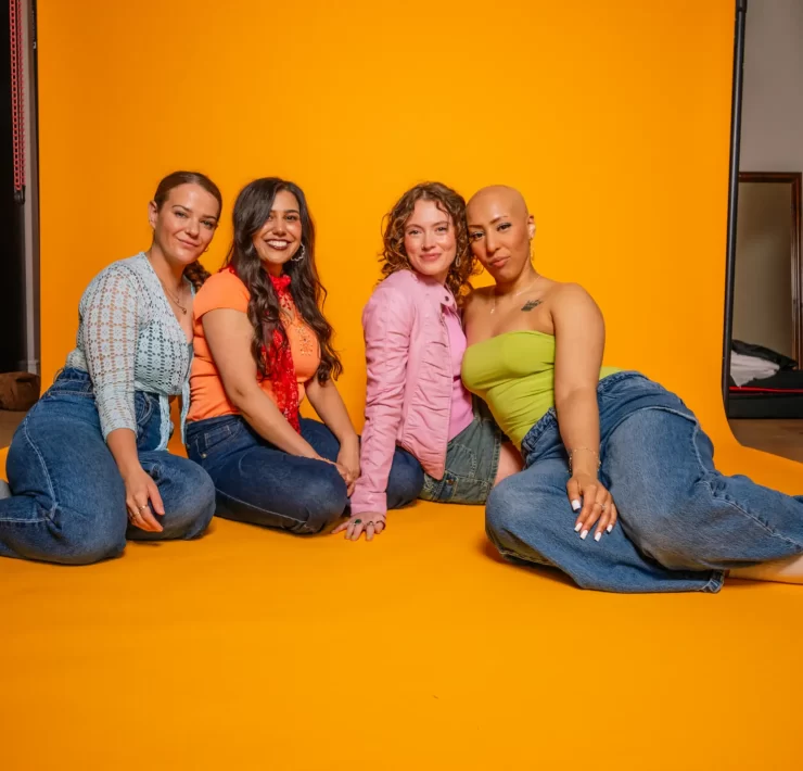 Four members of the Girl Pop! cast sitting together against a bright yellow backdrop, dressed in bold Y2K-inspired outfits.