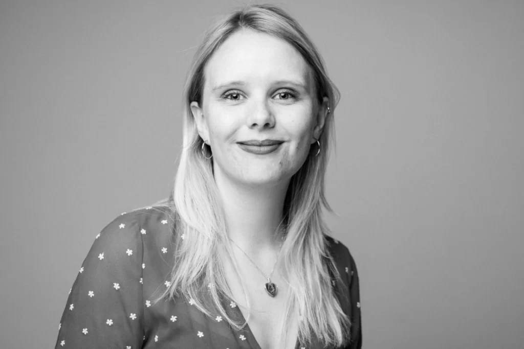 Black and white portrait of Sophie Cairns, wearing a floral dress and smiling at the camera.