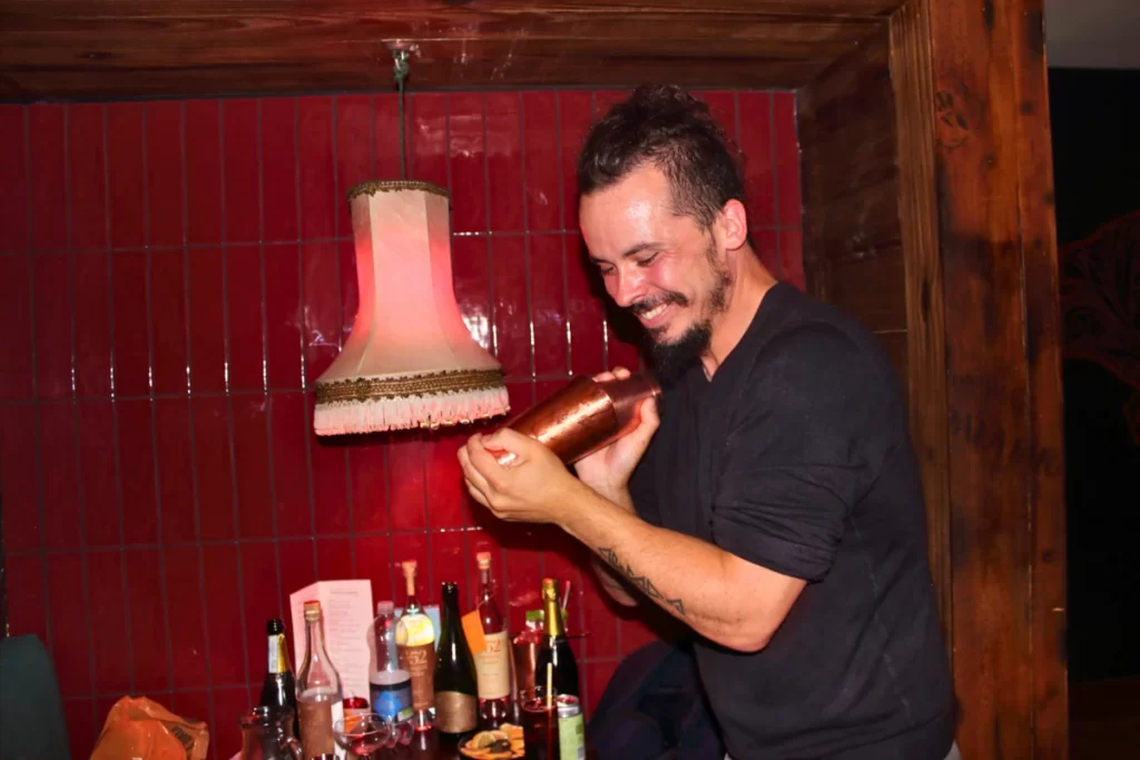 Bartender shaking a copper cocktail shaker under a red lamp.