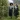 Two women in matching tartan skirts walking through a leafy garden path.