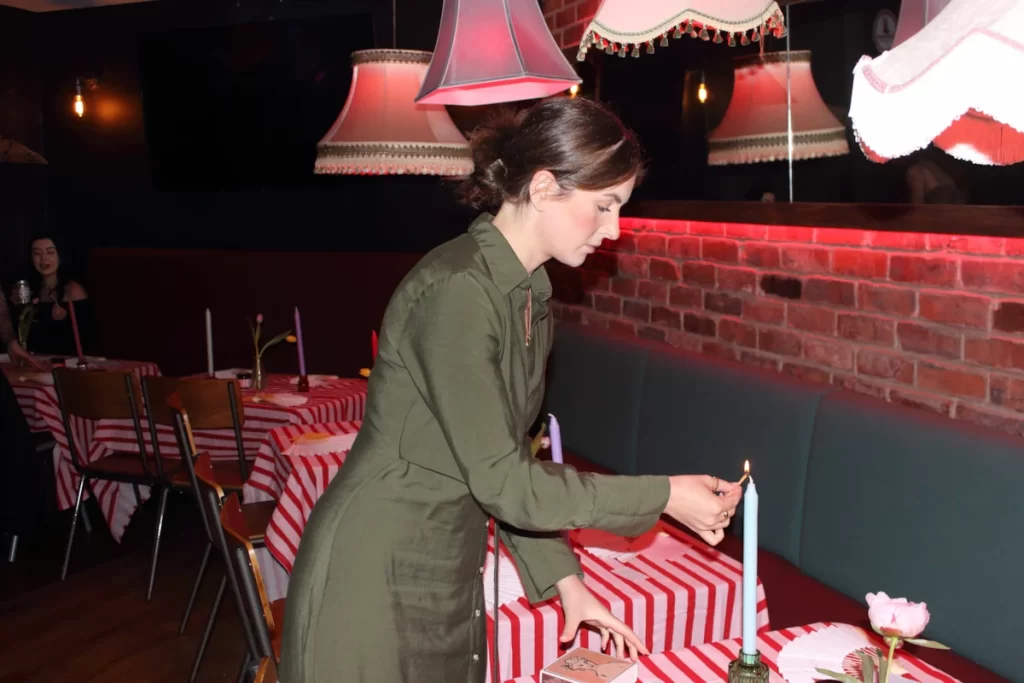 Woman lighting a tall candle on a striped table before the Quine event at Rioja Glasgow.