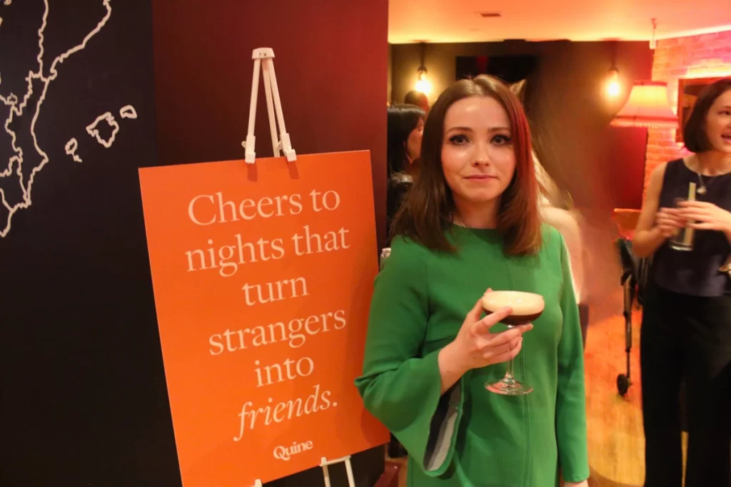 Woman in green holding an espresso martini beside a sign reading 'Cheers to nights that turn strangers into friends.'