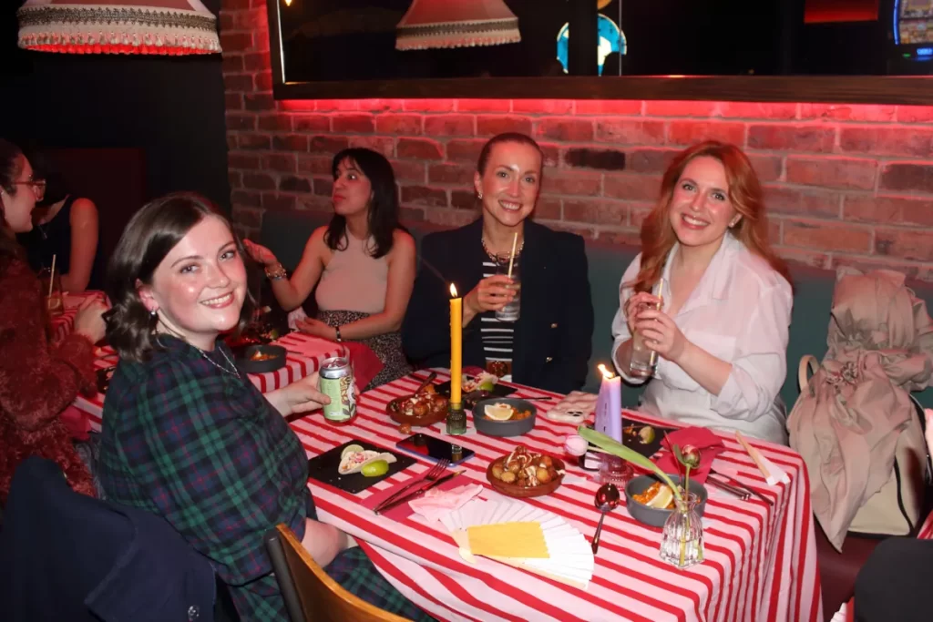 Three women smiling at a candlelit table covered in Spanish dishes and drinks in Glasgow.