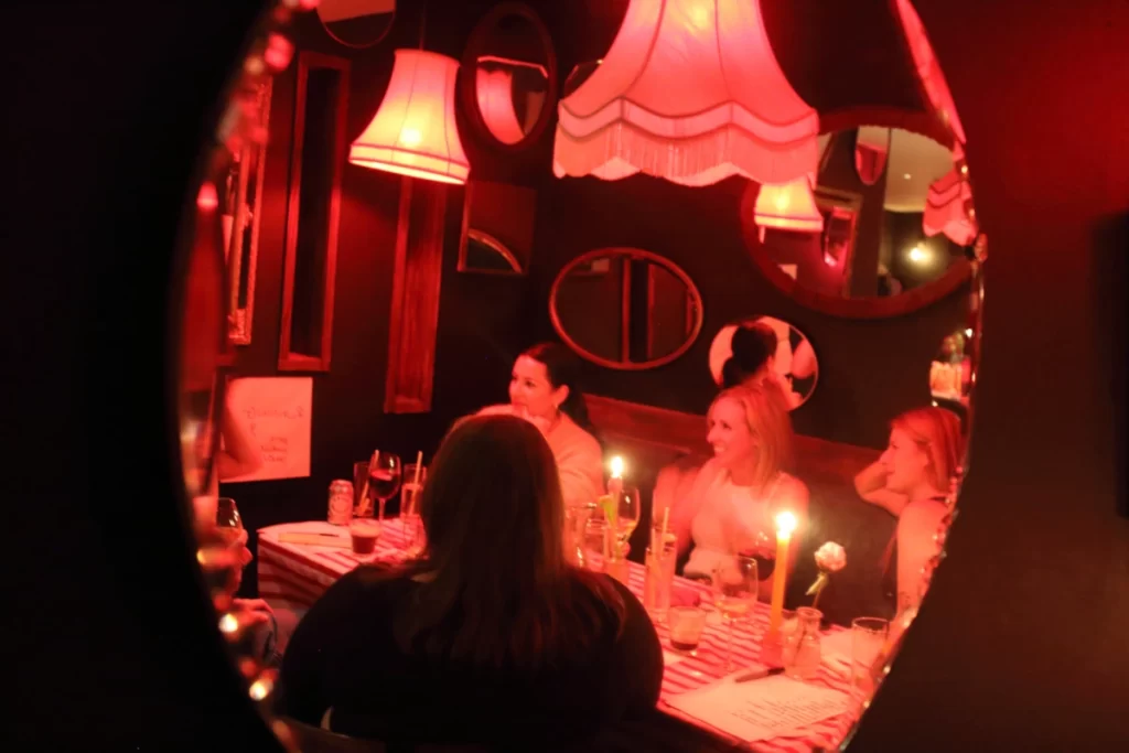 Candlelit supper club reflected in an oval mirror on a red wall.