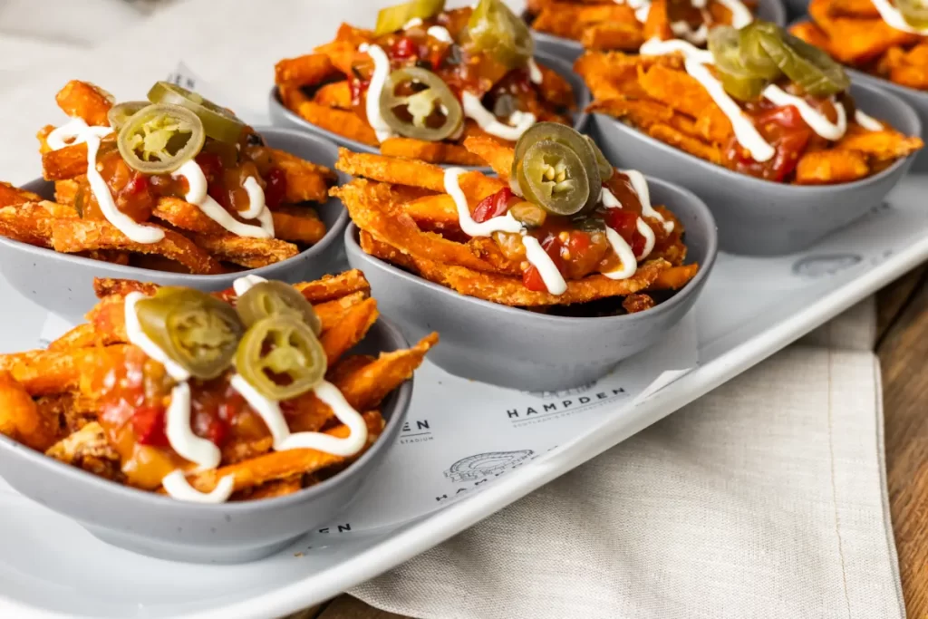 Close-up of loaded sweet potato fries with jalapeños, salsa, and sour cream served in small bowls.