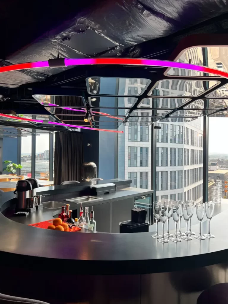 Close-up of the curved U-Bar at VEGA Glasgow with neon strip lighting, cocktail glasses and panoramic city views.