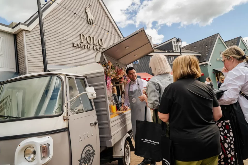 Man serving fizz to shoppers outside Polo Ralph Lauren at Caledonia Park VIP Shopping Weekend.