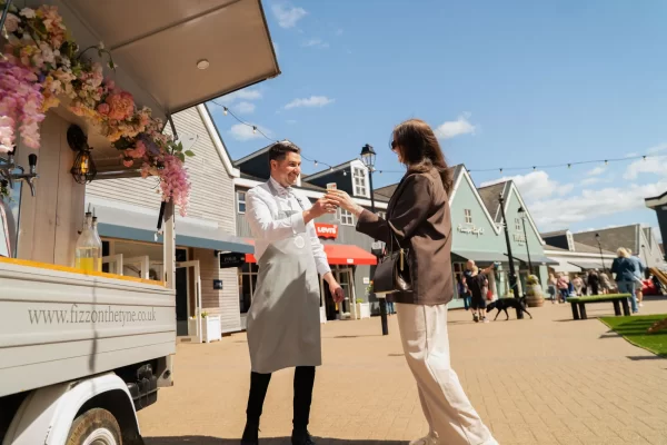 Man serving fizz to shopper at Caledonia Park outlet shopping village in Gretna Green.