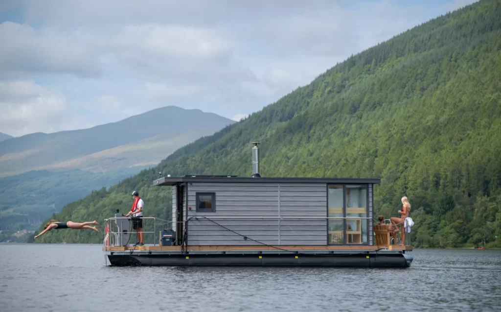 Woman diving into Loch Tay beside the Taymouth Marina HotBoat, a luxury floating sauna with views of Ben Lawers in the Scottish Highlands.