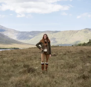 Model wearing Dubarry country boots, leggings, and a green jacket standing in a scenic Highland landscape with mountains and loch in the background.