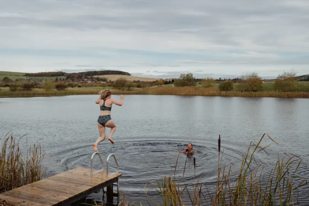 A woman jumps into a Scottish loch while another swimmer waits in the water.
