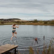 A woman jumps into a Scottish loch while another swimmer waits in the water.