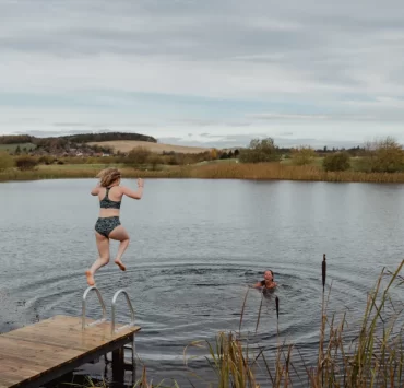 A woman jumps into a Scottish loch while another swimmer waits in the water.