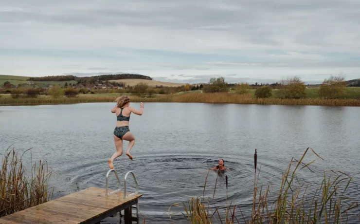 A woman jumps into a Scottish loch while another swimmer waits in the water.
