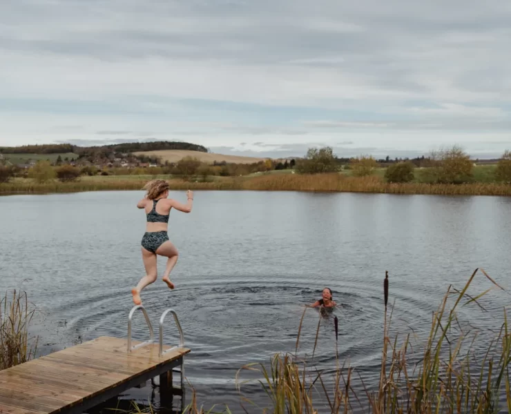A woman jumps into a Scottish loch while another swimmer waits in the water.