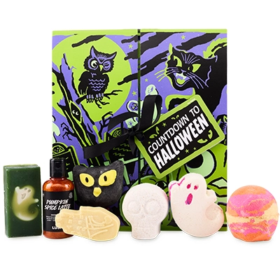 Lush Halloween Countdown box with neon green and purple design featuring an owl and cat illustration, shown with seven products – ghost soap, Pumpkin Spice Latte shower gel, cat bubble bar, skeleton bath bomb, ghost bath bomb, pumpkin scrub and gold bath bomb.