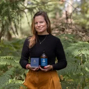 Laura Thomas, founder of Laura Thomas Co, holding the Balmoral Estate Woodland candle and hand wash surrounded by woodland greenery.
