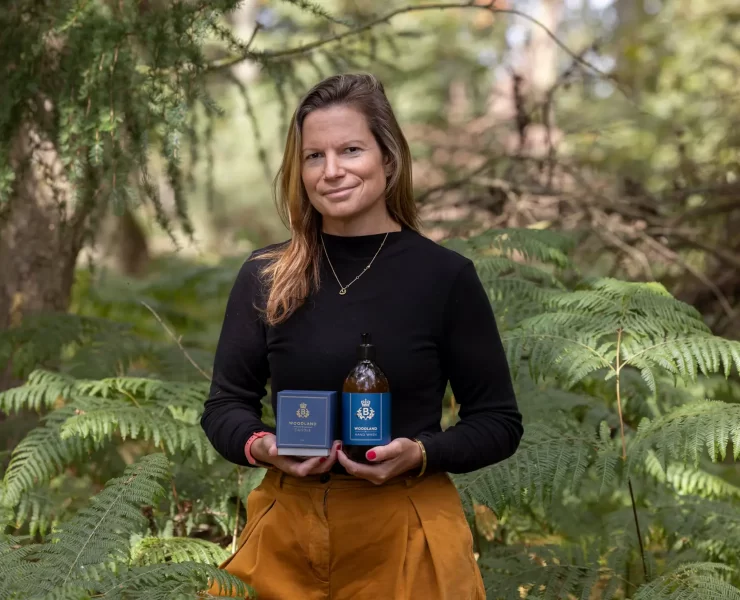 Laura Thomas, founder of Laura Thomas Co, holding the Balmoral Estate Woodland candle and hand wash surrounded by woodland greenery.