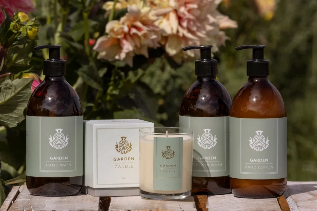 Laura Thomas Co Balmoral Garden Range with candle, hand wash, shower wash and lotion styled among flowers and greenery.