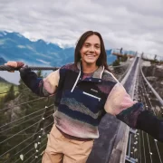 Woman wearing a colourful Columbia fleece outdoors on a mountain bridge, showcasing the brand’s performance outerwear collection.