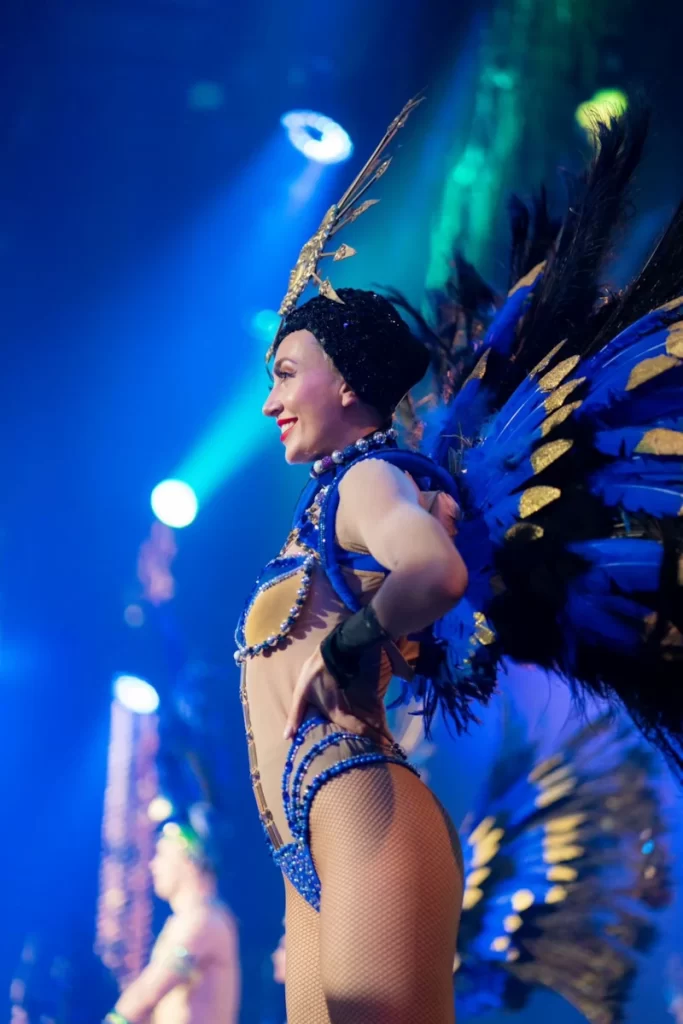 Cabaret dancer on stage at Trocadero’s, Crossbasket Castle in Scotland, wearing a blue and gold feathered costume with sparkling details, performing under stage lights.